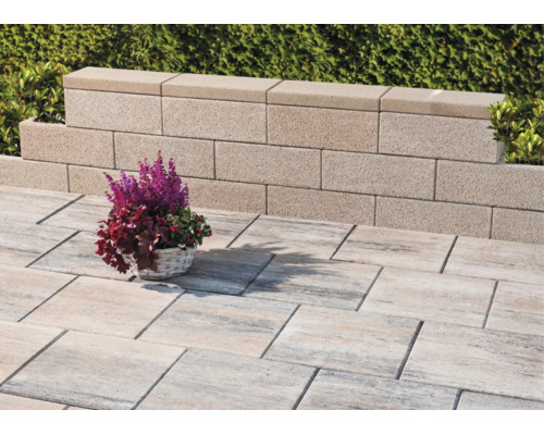 Helle Terrasse mit strukturierten, rechteckigen Bodenplatten und einer niedrigen Gartenmauer aus Betonsteinen.