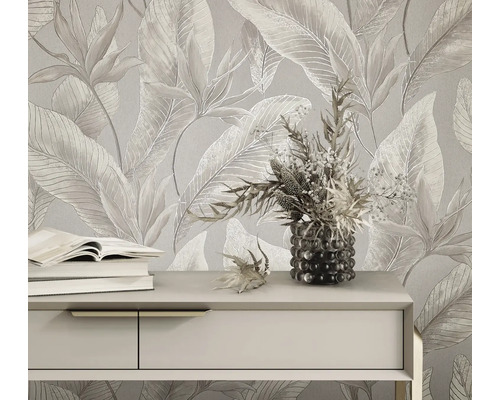 Helle Vliestapete mit großflächigem tropischem Blättermuster und Blüten hinter einem Sideboard mit Büchern und einer Blumenvase.