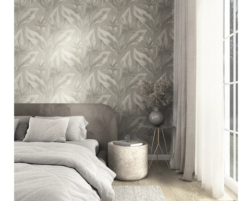 Schlafzimmer mit Vliestapete im botanischen Blättermuster, Bett mit Textilien und modernem Beistelltisch vor hellem Fenster.