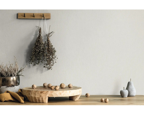 Hell strukturierte Wand mit rustikaler Dekoration, Holzbrett, Walnüssen, getrockneten Kräutern und Steinfrüchten auf einem Holztisch.
