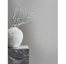 Minimalistisches Interieur mit grauer Wand, einer strukturierten Vase auf einem Marmorsockel und dekorativen Ästen.