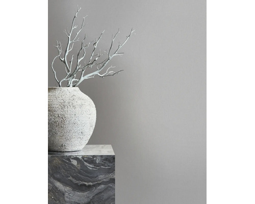 Minimalistisches Interieur mit grauer Wand, einer strukturierten Vase auf einem Marmorsockel und dekorativen Ästen.