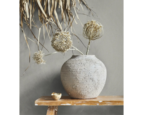 Rustikale Keramikvase mit strukturierter Oberfläche und getrockneten Blumen auf einer Holzbank vor einer Wand.