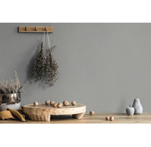 Graue Wand mit Struktur, dekoriert mit einem Wandhaken aus Holz, getrockneten Kräutern, einer Holzschale mit Walnüssen und Deko-Früchten.