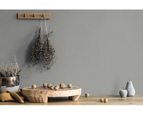 Graue Wand mit Struktur, dekoriert mit einem Wandhaken aus Holz, getrockneten Kräutern, einer Holzschale mit Walnüssen und Deko-Früchten.