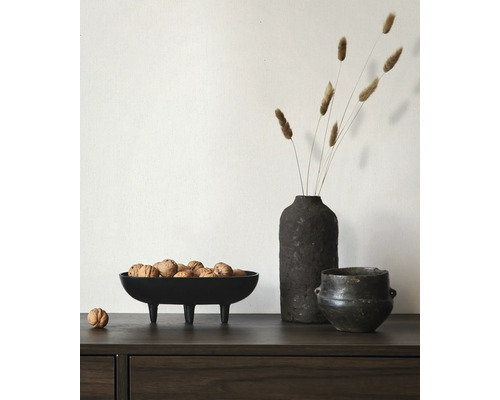 Schwarze dekorative Schale auf Beinen gefüllt mit Walnüssen neben einer dunklen strukturierten Vase mit Trockengräsern auf einer Holzkommode.