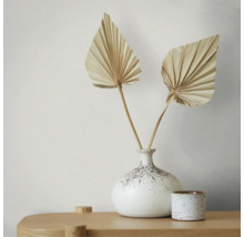 Zwei getrocknete fächerförmige Palmblätter in einer gesprenkelten Keramikvase auf einem hellen Holztisch, minimalistische und helle Dekoration.