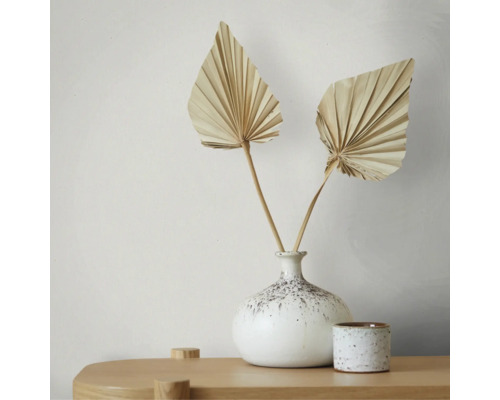 Zwei getrocknete fächerförmige Palmblätter in einer gesprenkelten Keramikvase auf einem hellen Holztisch, minimalistische und helle Dekoration.