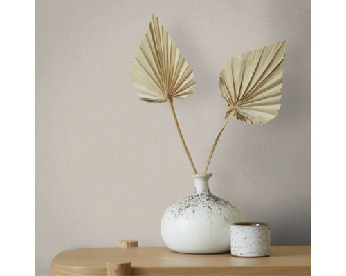 Minimalistische Dekoration mit gesprenkelter Keramikvase, zwei getrockneten Palmwedeln und kleinem Keramikgefäß auf einer Holzoberfläche.