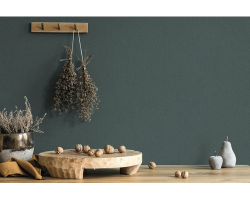 Dunkelgrün gestrichene Wand mit rustikaler Dekoration aus Holz, getrockneten Kräutern und Walnüssen auf einem Holztisch.