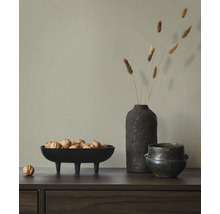 Hellgrüne strukturierte Vliestapete hinter einem Sideboard mit einer Schale Walnüssen, einer Vase mit Trockengras und einem dunklen Keramikgefäß.