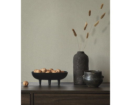 Hellgrüne strukturierte Vliestapete hinter einem Sideboard mit einer Schale Walnüssen, einer Vase mit Trockengras und einem dunklen Keramikgefäß.
