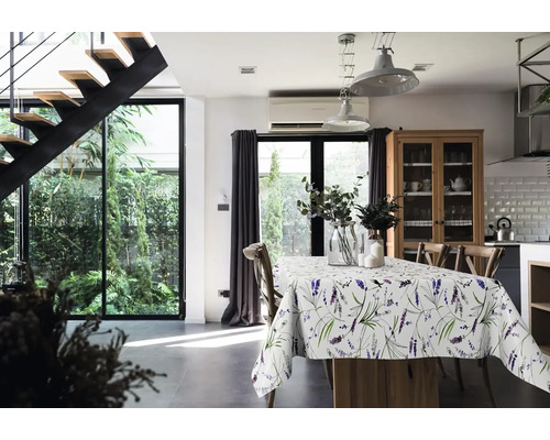 Helles Esszimmer mit Esstisch, Lavendel-Tischdecke, Holzstühlen, Industrie-Pendelleuchten und moderner schwarzer Treppe sowie Blick in den Garten.