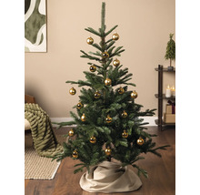 Künstlicher Weihnachtsbaum geschmückt mit goldenen Kugeln und beigefarbener Baumdecke in einem Wohnzimmer.