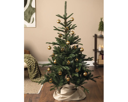 Künstlicher Weihnachtsbaum geschmückt mit goldenen Kugeln und beigefarbener Baumdecke in einem Wohnzimmer.