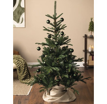 Kleiner grüner Weihnachtsbaum mit dunkelgrünen Christbaumkugeln in einem hellen, modern eingerichteten Wohnzimmer.