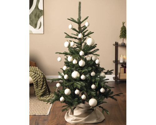 Grüner Weihnachtsbaum geschmückt mit weißen Christbaumkugeln in verschiedenen Größen und einer Baumdecke aus Stoff in einem modernen Wohnzimmer.