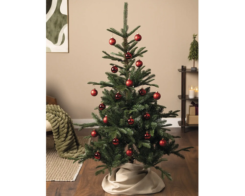 Künstlicher Tannenbaum dekoriert mit roten Christbaumkugeln in einem hellen Wohnzimmer auf Holzboden.