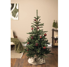 Grüner Weihnachtsbaum geschmückt mit roten Kugeln in einem gemütlichen Wohnzimmer mit Sessel, Regal und Weihnachtsdekoration.