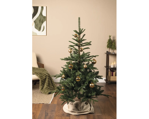 Künstlicher Tannenbaum mit goldenen Weihnachtskugeln in einem hellen Wohnzimmer mit Holzboden, beigem Teppich und gemütlicher Dekoration.