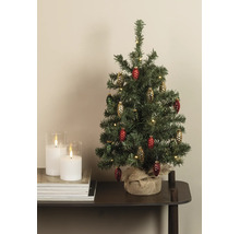 Kleiner künstlicher Weihnachtsbaum mit Zapfenanhängern und warmweißen Lichtern, Standfuß mit Jute umwickelt, auf einem Tisch neben Kerzen.