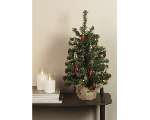Kleiner künstlicher Weihnachtsbaum mit Zapfenanhängern und warmweißen Lichtern, Standfuß mit Jute umwickelt, auf einem Tisch neben Kerzen.