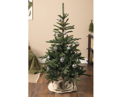Künstlicher Weihnachtsbaum mit silbernen Kugeln mit Schneeflockenmuster auf Holzboden in einem organisierten Wohnbereich.