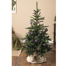 Ein Weihnachtsbaum dekoriert mit lila Christbaumkugeln mit weißem Schneeflockenmuster, stehend auf einem Holzboden.