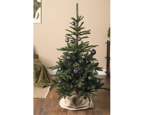 Ein Weihnachtsbaum dekoriert mit lila Christbaumkugeln mit weißem Schneeflockenmuster, stehend auf einem Holzboden.