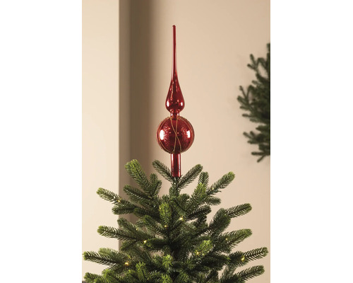 Christbaumspitze aus Glas in Rot auf der Spitze eines beleuchteten Weihnachtsbaums.