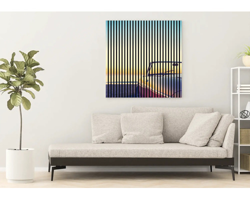 Modernes, helles Wohnzimmer mit minimalistischem Sofa, einer großen Zimmerpflanze und einem quadratischen Wandbild mit Auto-Motiv hinter Streifen.