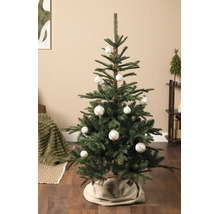 Hell dekorierter künstlicher Weihnachtsbaum in einem Wohnzimmer, geschmückt mit weißen Christbaumkugeln mit Karomuster und einer beigen Baumdecke.