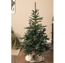 Grüner Weihnachtsbaum geschmückt mit blau gemusterten Weihnachtskugeln auf einem Holzboden mit einer beigen Christbaumdecke.