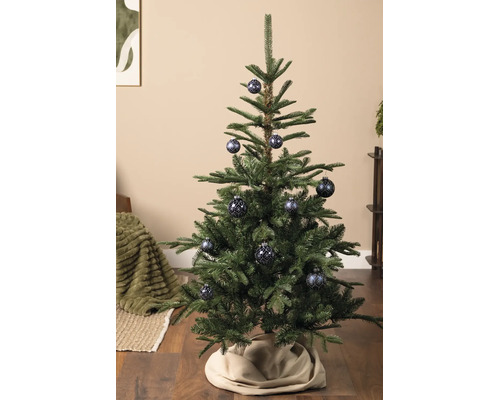Grüner Weihnachtsbaum geschmückt mit blau gemusterten Weihnachtskugeln auf einem Holzboden mit einer beigen Christbaumdecke.