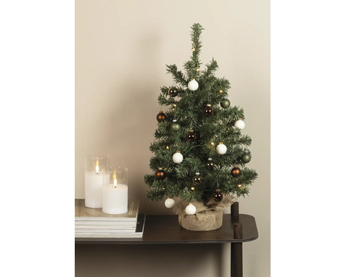 Kleiner künstlicher Weihnachtsbaum mit LED-Beleuchtung und Kugeln, Standfuß mit Jute umwickelt, auf einem Tisch neben Kerzen.
