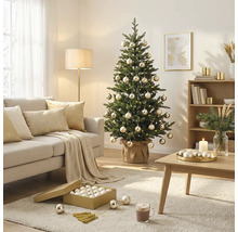 Geschmückter Weihnachtsbaum mit Kugeln und Lichterkette in einem hellen Wohnzimmer mit Sofa, Couchtisch und Teppich.