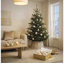 Geschmückter Christbaum in hellem Wohnzimmer mit beigem Sofa, Holzcouchtisch und festlichem Christbaumschmuck.