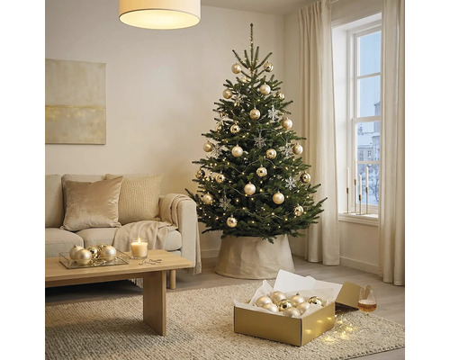 Geschmückter Christbaum in hellem Wohnzimmer mit beigem Sofa, Holzcouchtisch und festlichem Christbaumschmuck.