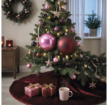 Festlich dekorierter Weihnachtsbaum mit großen und kleinen Kugeln, Sternen und Lichterkette auf einer dunkelroten Samt-Baumdecke mit Geschenken.