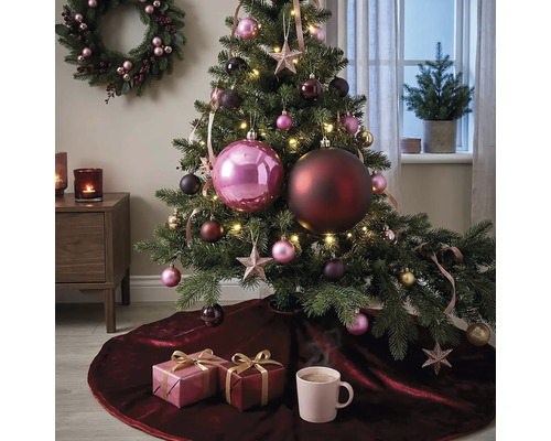 Festlich dekorierter Weihnachtsbaum mit großen und kleinen Kugeln, Sternen und Lichterkette auf einer dunkelroten Samt-Baumdecke mit Geschenken.