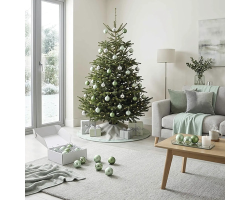 Festlich geschmückter Christbaum in einem hellen Wohnzimmer mit Sofa, Couchtisch aus Holz sowie silbernen und grünen Christbaumkugeln.