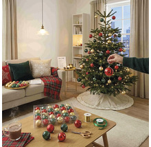 Hell gestaltetes Wohnzimmer mit einem geschmückten Weihnachtsbaum, Sofa mit Kissen und einem Couchtisch mit Weihnachtskugeln und Bastelutensilien.