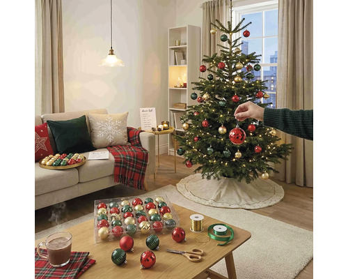 Hell gestaltetes Wohnzimmer mit einem geschmückten Weihnachtsbaum, Sofa mit Kissen und einem Couchtisch mit Weihnachtskugeln und Bastelutensilien.