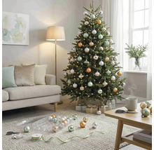 Festlich geschmückter Weihnachtsbaum mit silbernen, goldenen und salbeigrünen Kugeln sowie Lichterkette in einem hellen Wohnzimmer.