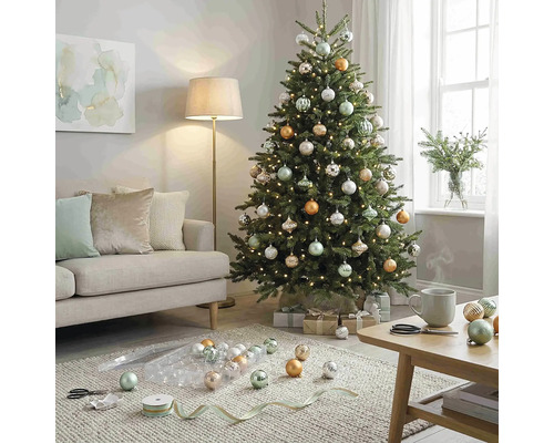 Festlich geschmückter Weihnachtsbaum mit silbernen, goldenen und salbeigrünen Kugeln sowie Lichterkette in einem hellen Wohnzimmer.
