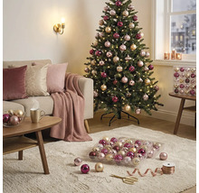 Heller, gemütlicher Wohnbereich mit einem geschmückten Weihnachtsbaum, einem Sofa mit Kissen und einem Teppich mit Christbaumschmuck.