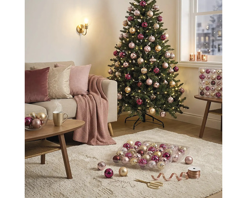 Heller, gemütlicher Wohnbereich mit einem geschmückten Weihnachtsbaum, einem Sofa mit Kissen und einem Teppich mit Christbaumschmuck.