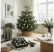 Festlich geschmückter Christbaum in einem hellen Wohnzimmer mit Couch, Holztisch und Christbaumschmuck.