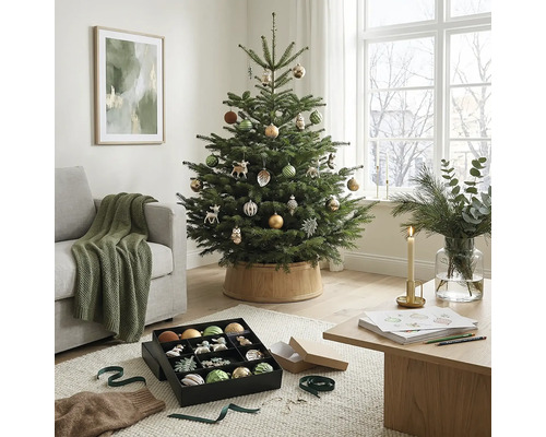 Festlich geschmückter Christbaum in einem hellen Wohnzimmer mit Couch, Holztisch und Christbaumschmuck.