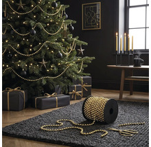 Weihnachtsbaum dekoriert mit goldfarbener Perlenkette, Spule mit Perlenkette im Vordergrund auf einem dunklen Teppich.